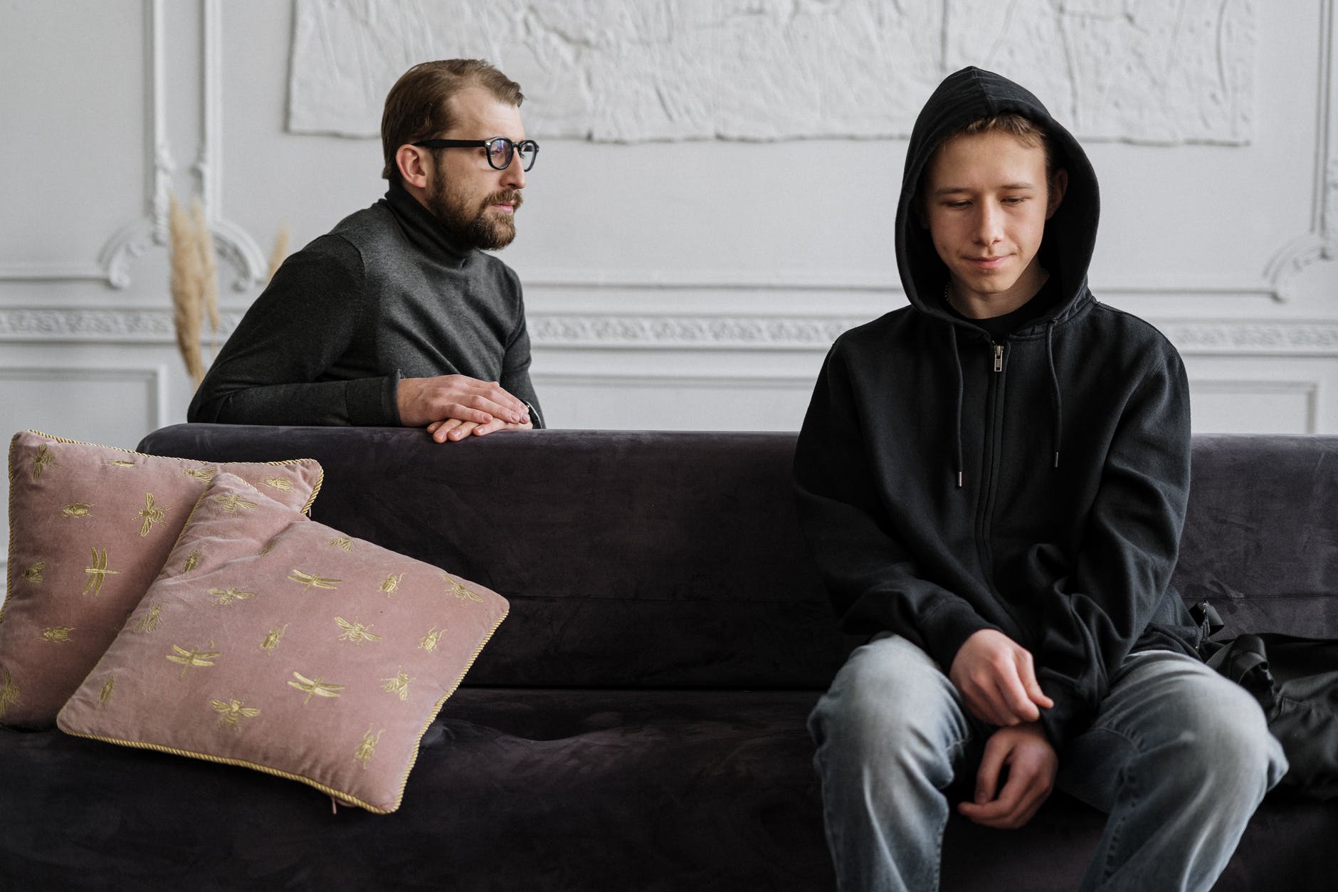 man in black hoodie sitting on brown couch